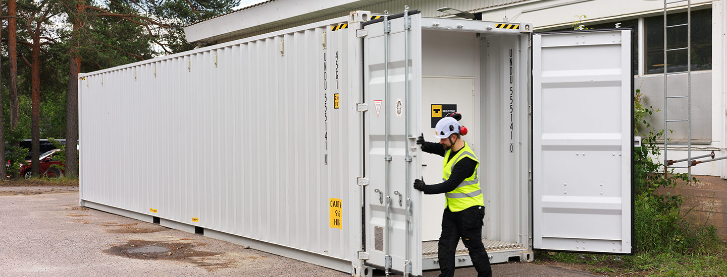 Merikontti, jonka ovea työvaatteisiin pukeutunut henkilö avaa. Merikonttiin on rakennettu itsepalvelu kaupintavarasto, joka toimii RFID:llä