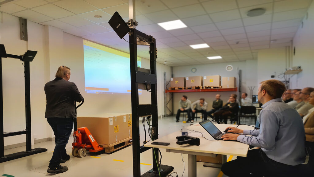 A person demonstrating an RFID gate in a Turck Vilant Systems demo showroom, while several attendees watch.