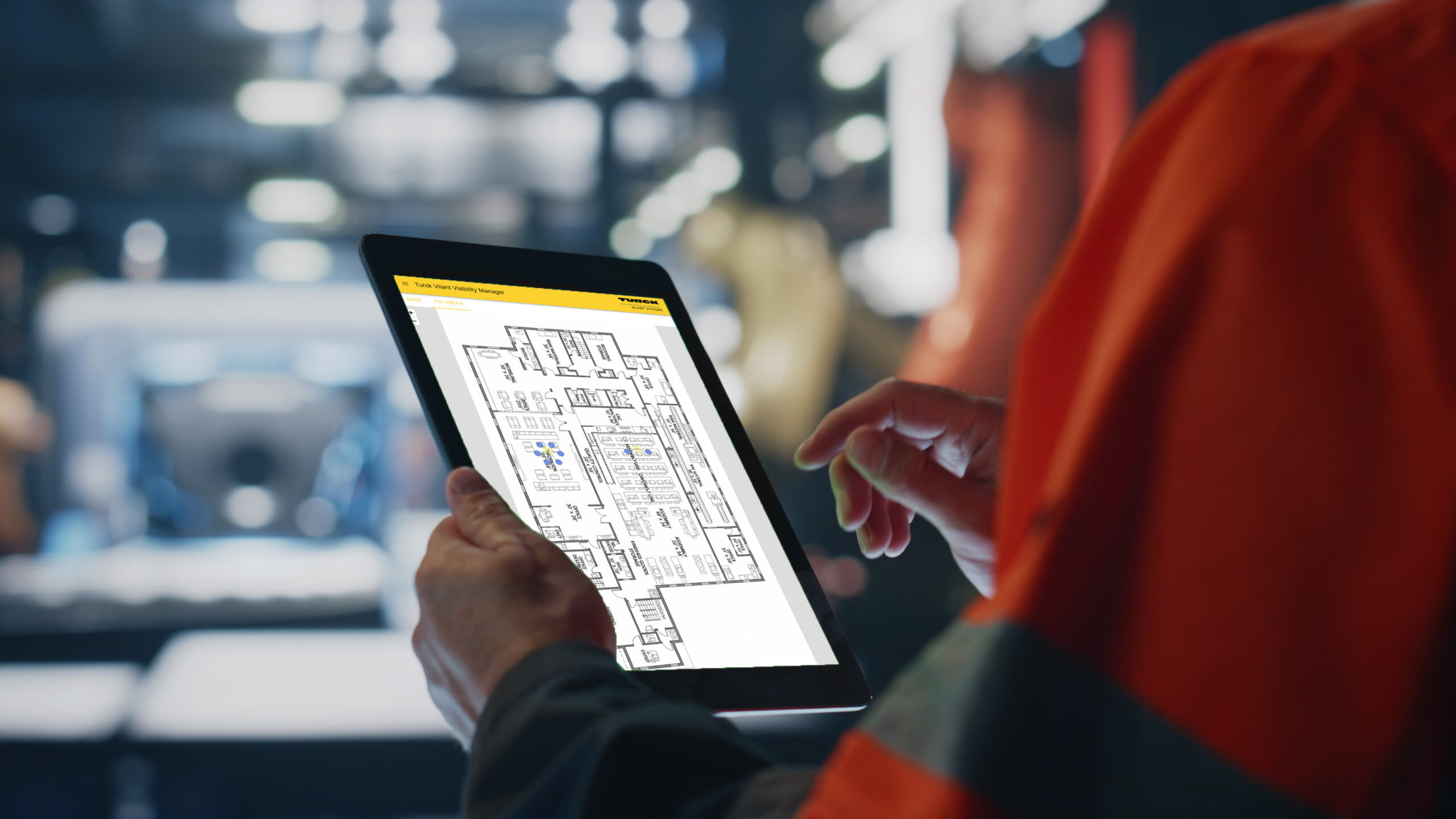 Person looking at a tablet in a factory, tablet screen showcases a floor plan with data for finding assets on the floor plan - RFID used for tracking the assets