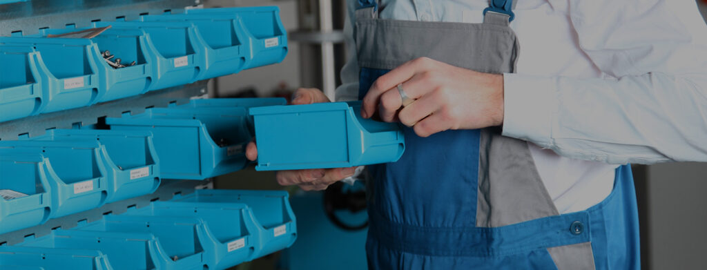 Plastic bins on a rack on the background, a person holding one of them on the foreground showcasing how RFID-based-kanban ensures item availability in production