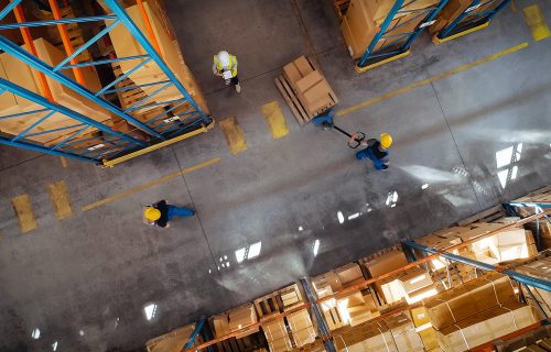 RFID and RTLS track inventory in warehouses Birdseye view of a large warehouse with employees depicted from above