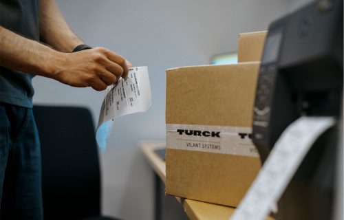 TVS-rfid-tagging-process A person labelling cartons with an RFID tag with RFID printer in the front